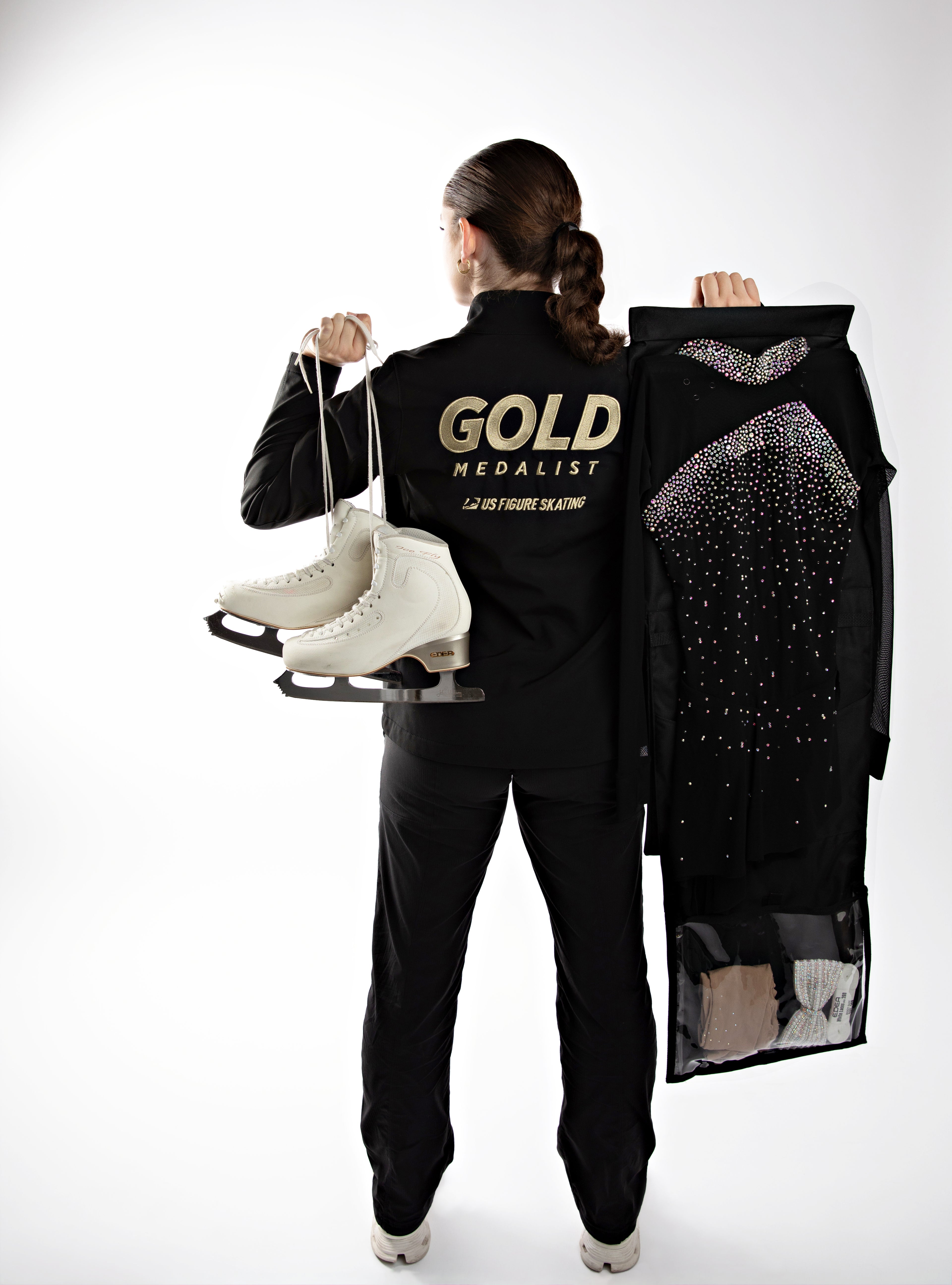 Person holding ice skates and a decorative bag with 'Gold Medalist' branding on a white background