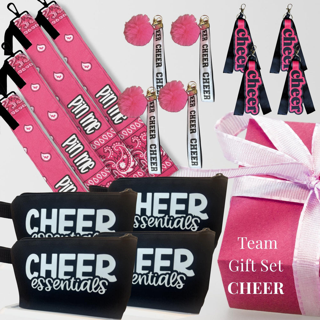 Pink cheer bag tags, pom keychains, black zipper pouches labeled Cheer Essentials, and a pink cheer bow with ribbon.