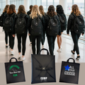 Group of people walking with black backpacks in a modern building, with additional black bags displayed below.