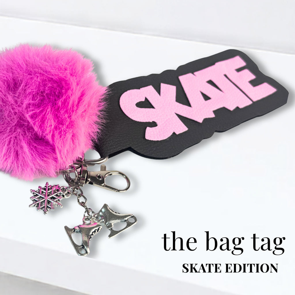 Black bag tag with pink "SKATE" text, attached to silver ice skate and snowflake charms, and a pink fluffy pom-pom keychain.