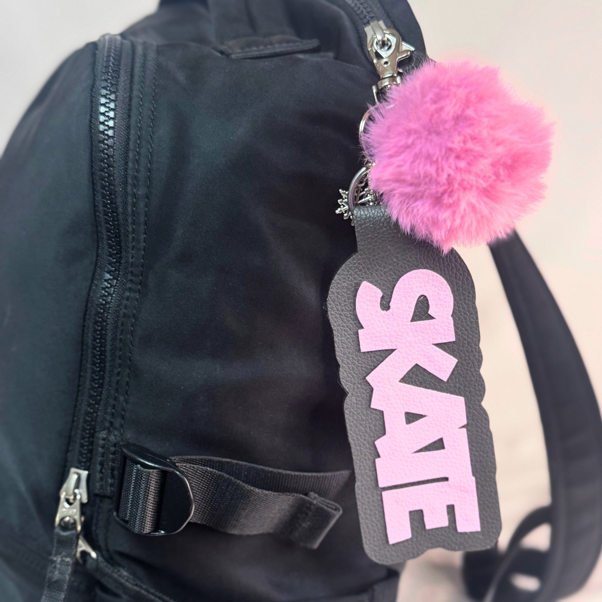 Black skate bag with pink "SKATE" bag tag and fluffy pink pom-pom cheer accessory.