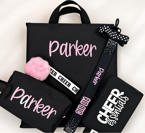 Black cheer backpack set with pink personalized name, pom pom keychain, bow hair tie, and cheer emergency kit pouch.