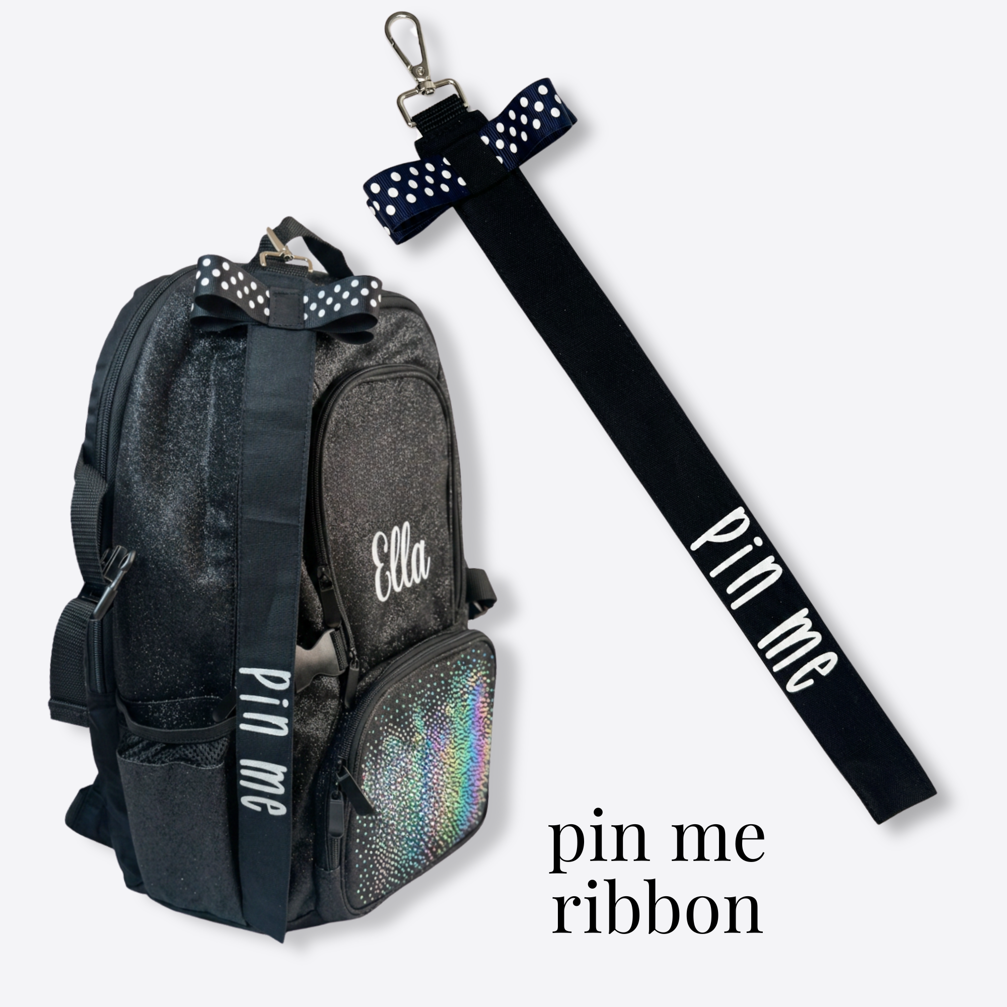 Black cotton Pin Me ribbon with white polka dot bow and "pin me" text, clipped to a black cheer backpack with holographic.