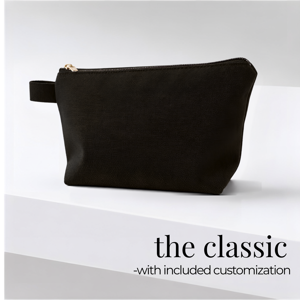 A black textured pouch with a gold zipper and a small side loop, shown on a clean white and light gray background with the text 'the classic -with included customization' at the bottom right.
