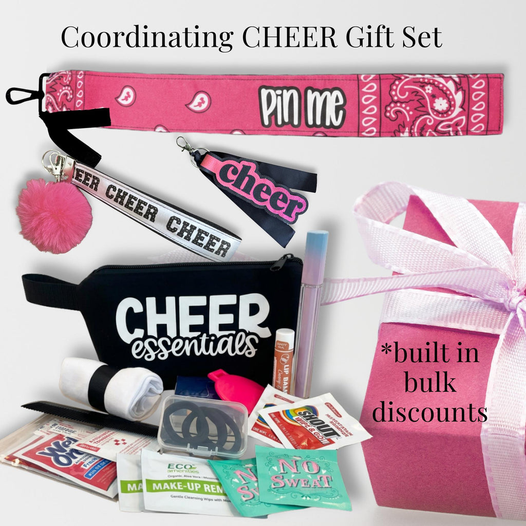 Pink cheer bag tag with bandana design, black cheer essentials wristlet, cheer pom pom keychain, lip gloss, and pink ribbon.