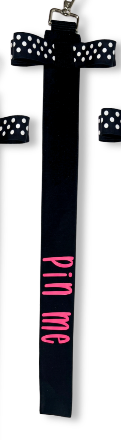 Black cotton ribbon with white polka dot bow and pink "pin me" text, cheer accessory for bag or uniform.