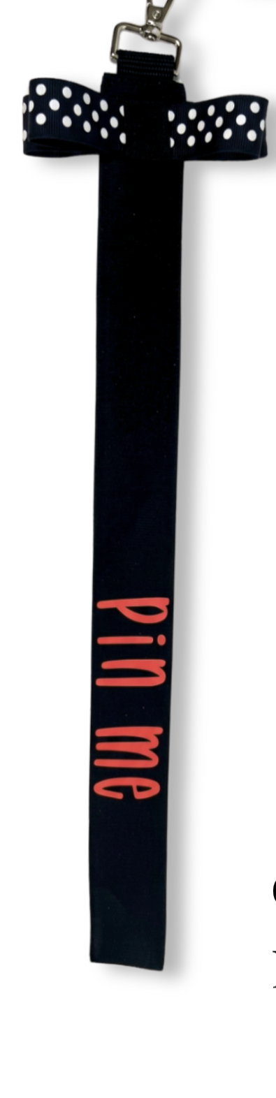 Black cotton ribbon pin with white polka dots and pink "pin me" text, metal clip attached.