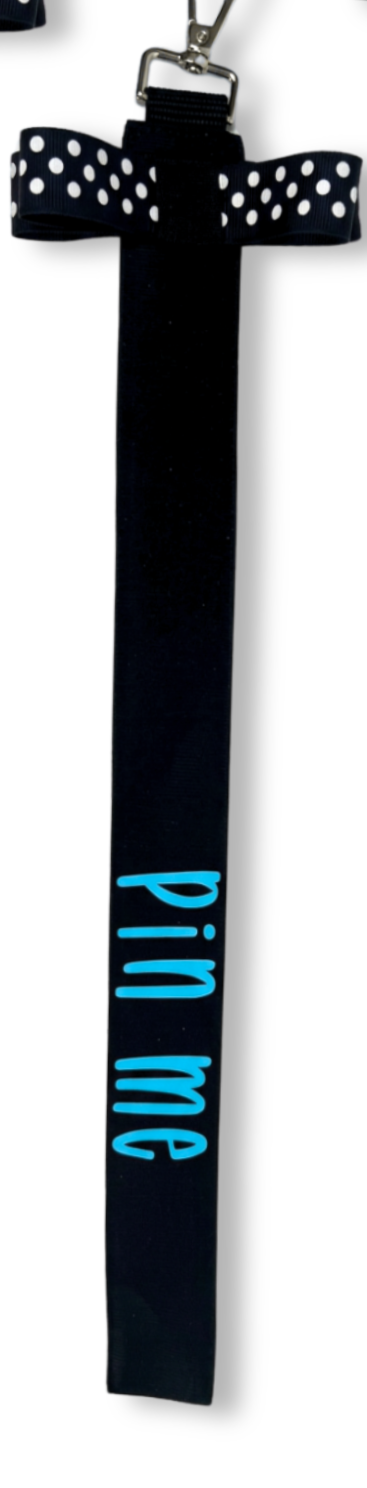 Black cotton ribbon bag tag with white polka dot bow and blue "pin me" text hanging from metal clip.